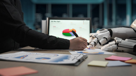 A human hand drawing on paper while a robotic hand assists, showcasing a modern office environment focused on data visualization and productivity in business analytics.の写真素材