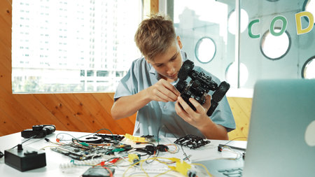 Highschool boy fixing car model with laptop and electric tool placed on table. Closeup of teenager...