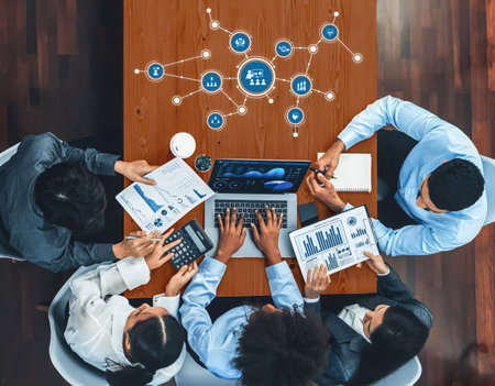 A diverse business team engaged in a strategic meeting around a modern office table, analyzing data and exchanging ideas using advanced technology and collaborative tools.の写真素材