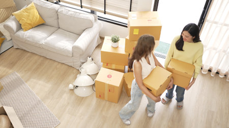 Couple of woman carrying box and arriving at new house at moving day. Top view of beautiful girl and...