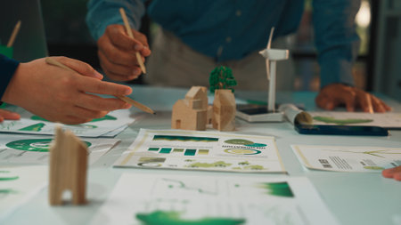 This image captures a collaborative design session where a team focuses on sustainable architecture, showcasing models, sketches, and eco-friendly concepts on a table.の写真素材
