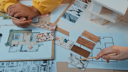 Hands examining color samples and floor plans, showcasing the collaborative and creative process of interior design and home renovation planning for artistic projects.の写真素材