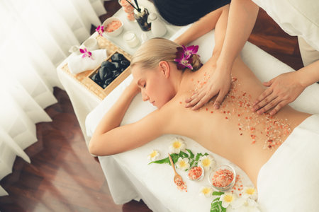 Woman customer having exfoliation treatment in luxury spa salon with warmth candle light ambient. Salt scrub beauty treatment in health spa body scrub. Quiescentの写真素材