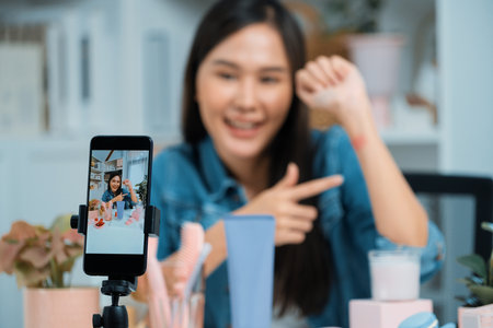 Young beautiful Asian showing cosmetic makeup lipstick matte pastel color testing in bestseller collection on arm test promotion on social media online recording smartphone at modern room.の写真素材