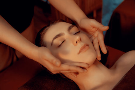 Caucasian woman enjoying relaxing anti-stress head massage and pampering facial beauty skin recreation leisure in warm candle lighting ambient salon spa in luxury resort or hotel. Quiescentの写真素材