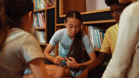 Group of diverse children sitting in circle while reading a book at library. Highschool girl sharing...