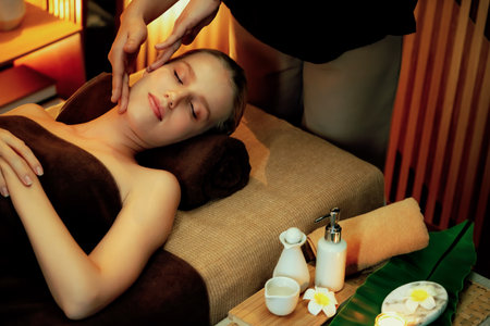 Caucasian woman enjoying relaxing anti-stress head massage and pampering facial beauty skin recreation leisure in warm candle lighting ambient salon spa in luxury resort or hotel. Quiescentの写真素材