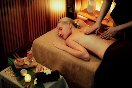 Woman customer having exfoliation treatment in luxury spa salon with warmth candle light ambient. Salt scrub beauty treatment in Health spa body scrub. Quiescentの写真素材