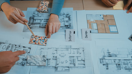Hands of designers actively engaging in a collaborative session to select color swatches and analyze architectural plans on the table for an interior design project.の写真素材