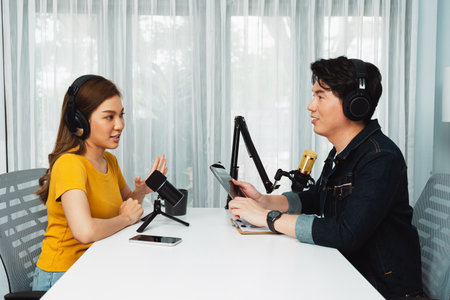Smiling radio influencer host holding tablet wearing headphones interview woman speaker social media online live streaming channel with talking to share link at morning at studio record. Infobahn.のeditorial素材