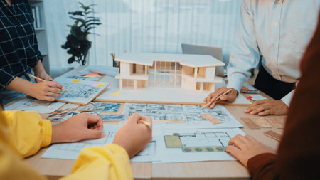 A group of architects and designers engage in a collaborative design session, surrounded by architectural plans and a detailed model. The bright office fosters creativity. SACTRのeditorial素材