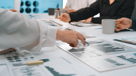 A dynamic business meeting showcasing hands pointing at graphs and charts on a table, highlighting data analysis and collaborative discussions among professionals. SACTRのeditorial素材