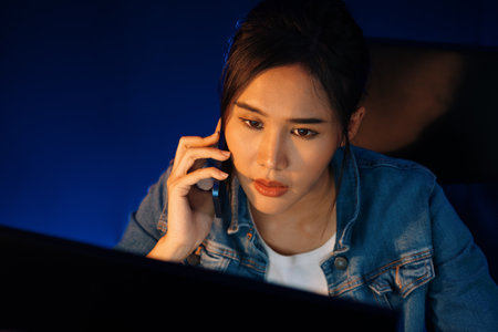 Young Asian woman calling on phone to customer or coworker while searching market analysis on pc at...