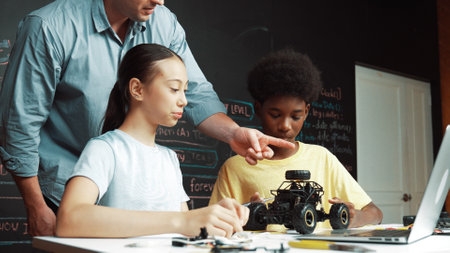 Teacher talking about electric tool while student fixing robotic model on table with electronic equipment placed. Diverse academic children learning about main board structure.の写真素材