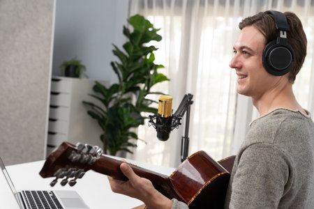 Host channel with smiling face, playing guitar along singing, broadcasting on social media channel, wearing headphones to record video streamer at modern studio recording.の写真素材