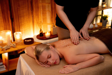 Woman customer having exfoliation treatment in luxury spa salon with warmth candle light ambient. Salt scrub beauty treatment in Health spa body scrub. Quiescentの写真素材