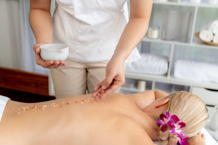 Woman customer having exfoliation treatment in luxury spa salon with warmth candle light ambient. Salt scrub beauty treatment in health spa body scrub. Quiescentの写真素材
