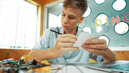 Smart happy boy inspect or learning to use electronic tool while taking a note. Happy highschool...