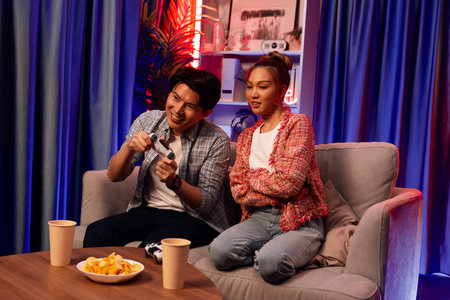 Sitting sofa of happy couple playing video game with joysticks, smiling man playing challenge,...