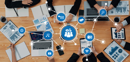 A dynamic business meeting scene showcasing teamwork and technology, with laptops, tablets, and documents spread on a wooden table emphasizing data analysis and collaboration.の写真素材