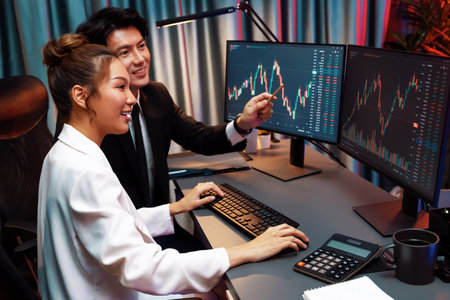 Smiling Asian business traders pointing to dynamic stock exchange data screen profit value online...