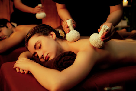 Hot herbal ball spa massage body treatment, masseur gently compresses herb bag on couple customer body. Serenity of aromatherapy recreation in warm lighting of candles at spa salon. Quiescentの写真素材