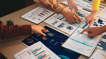 A group of professionals engaging in collaborative analysis over various business charts and graphs on a desk, highlighting teamwork and strategic discussions in a modern office environment.の写真素材