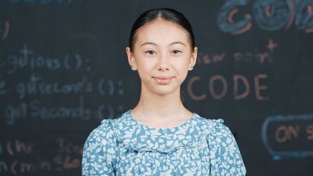 Cute caucasian girl looking at camera while standing at blackboard with engineering prompt. Skilled...