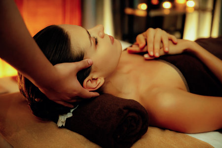 Caucasian woman enjoying relaxing anti-stress head massage and pampering facial beauty skin recreation leisure in warm candle lighting ambient salon spa in luxury resort or hotel. Quiescentの写真素材