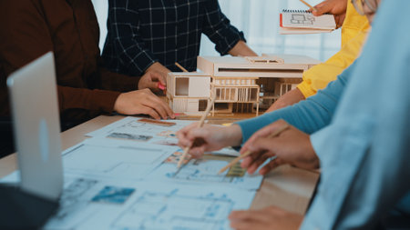 A diverse team engages in brainstorming and planning an architectural project. The scene showcases hands working on models and drawings in a creative workspace environment.の写真素材
