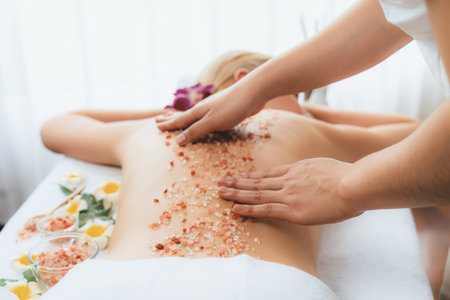 Closeup woman customer having exfoliation treatment in luxury spa salon with warmth candle light ambient. Salt scrub beauty treatment in health spa body scrub. Quiescentの写真素材