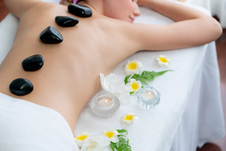 Hot stone massage at spa salon in luxury resort with day light serenity ambient, blissful woman customer enjoying spa basalt stone massage glide over body with soothing warmth. Quiescentの写真素材