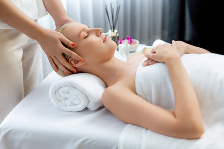 Caucasian woman enjoying relaxing anti-stress head massage and pampering facial beauty skin recreation leisure in dayspa modern light ambient at luxury resort or hotel spa salon. Quiescentの写真素材