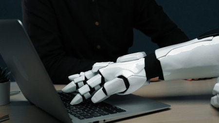 A robotic hand engages with a laptop, representing the convergence of technology and human...