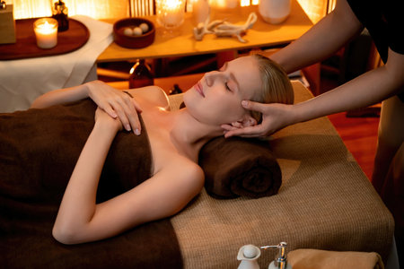 Caucasian woman enjoying relaxing anti-stress head massage and pampering facial beauty skin recreation leisure in warm candle lighting ambient salon spa in luxury resort or hotel. Quiescentの写真素材