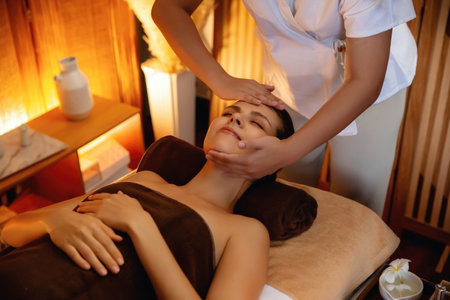Caucasian woman enjoying relaxing anti-stress head massage and pampering facial beauty skin recreation leisure in warm candle lighting ambient salon spa in luxury resort or hotel. Quiescentの写真素材