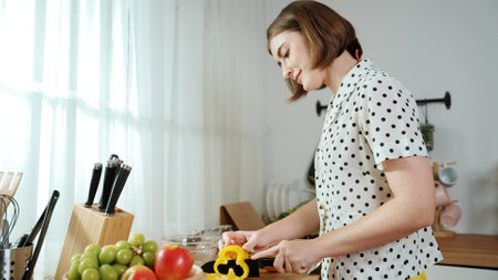 Energetic mother making salad for breakfast at modern kitchen while chopping vegetable surrounded with kitchenware. Smart female house keeper cooking and preparing food. Healthy lifestyle. Pedagogy.の写真素材