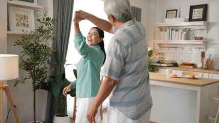 Happy grandfather and grandmother with casual cloth holding hand and dancing together at home. Lovely senior couple moving to music and spending time together while supporting at kitchen.の写真素材