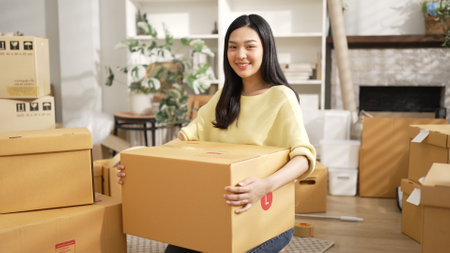 Young female business owner holding cardboard while standing at shop. Attractive happy entrepreneur...
