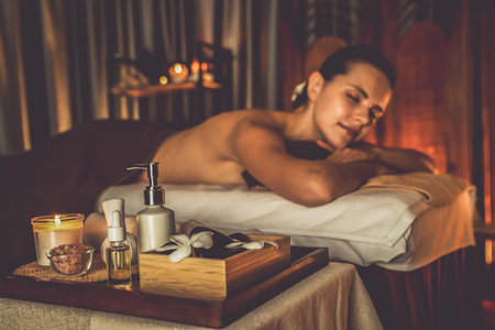 Aromatherapy massage ambiance or spa salon composition setup with focus decor candles and spa accessories on blurred woman enjoying blissful aroma spa massage in resort or hotel background. Quiescentの写真素材