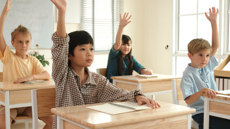 Smart boy raising hand for asking and answering teacher surrounded by multicultural children studying at classroom. Happy student working together, voting, volunteering, calling instructor. Pedagogy.の写真素材