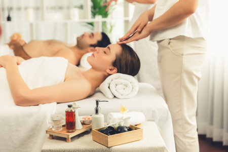 Caucasian couple enjoying relaxing anti-stress head massage and pampering facial beauty skin recreation leisure in dayspa modern light ambient at luxury resort or hotel spa salon. Quiescentの写真素材