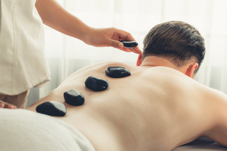 Hot stone massage at spa salon in luxury resort with day light serenity ambient, blissful man customer enjoying spa basalt stone massage glide over body with soothing warmth. Quiescentの写真素材