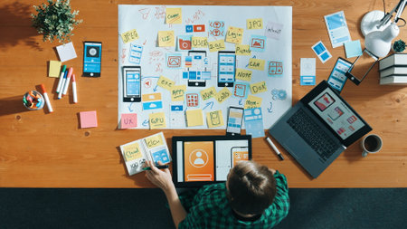 Top view of smart developer working on tablet and writing Ux Ui design for mobile phone interface at...