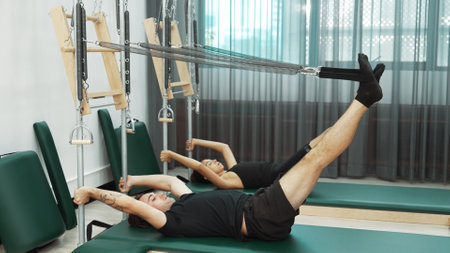Group of clients performing Pilates exercises on Cadillac reformer machine for improving core...