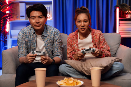 Sitting sofa of happy smiling couple playing video game control by joystick fronted snack and drinks...