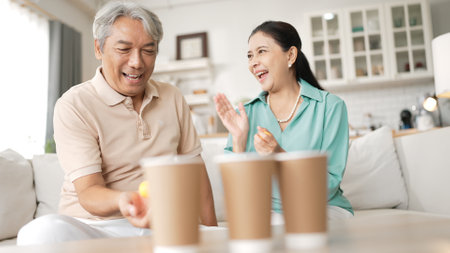 Happy elderly couple enjoying a ball toss game together at home, practicing coordination and cognitive skills for healthy aging. Grandfather and grandmother throwing ping pong in the bowl.の写真素材