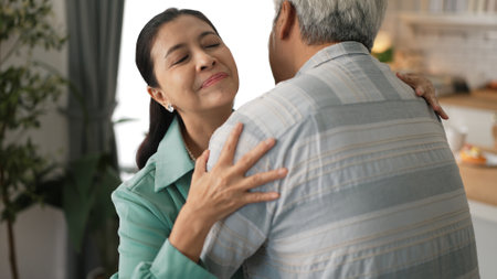 Happy grandfather and grandmother with casual cloth holding hand and dancing together at home. Lovely senior couple moving to music and spending time together while supporting at kitchen.の写真素材