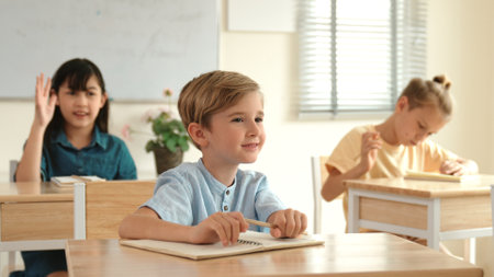 Smart elementary student looking at teacher while attend in classroom. Diverse smart student sitting...