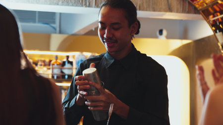 Asian bartender shaking mixed cocktail preparing presentation to serve beautiful woman guest at...
